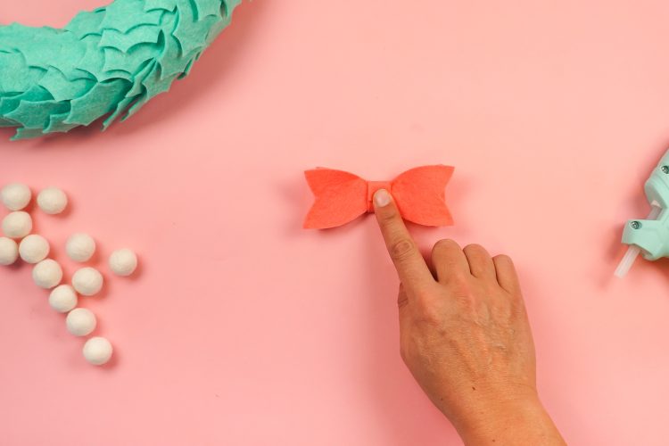 Image of hands using glue gun to glue together the parts of a bow for the wreath