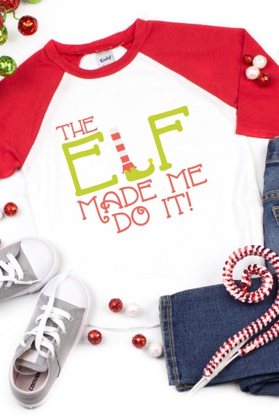 Christmas jingle bells around a pair of blue jeans, tennis shoes and a baseball style pink and white shirt that says, "The Elf Made Me Do It"