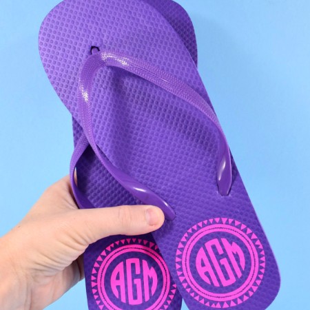 A woman holding a pair of purple monogramed flip flops
