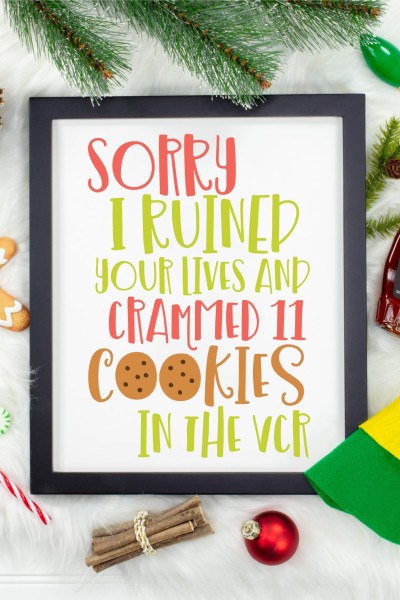 Christmas decor around a wooden framed sign with the quote "Sorry I Ruined Your Lives and Crammed 11 Cookies in the VCR"