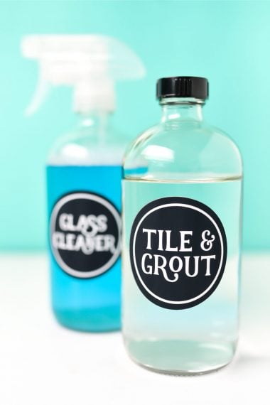 A glass bottle with the label "Tile & Grout" on it and a spray bottle with the label "Glass Cleaner