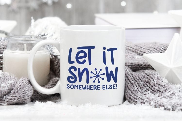 A coffee cup on a table with the saying \"Let IT Snow Somewhere Else\"