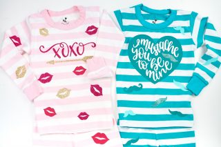 Two pair of infant pj's - one pink and white striped with vinyl cut outs of red and gold lips, an arrow and xoxo applied to the pajama top and bottom and a blue and white striped one with mustaches applied to the pajama top and bottom with the top having a heart with the saying, "I mustache you to be mine".