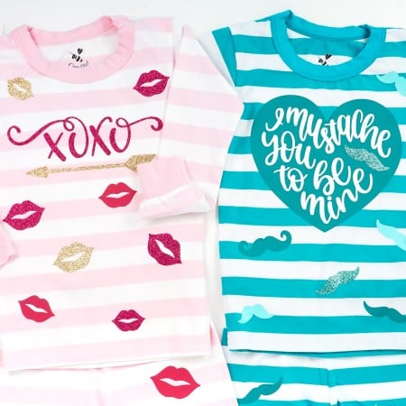 Two pair of infant pj's - one pink and white striped with vinyl cut outs of red and gold lips, an arrow and xoxo applied to the pajama top and bottom and a blue and white striped one with mustaches applied to the pajama top and bottom with the top having a heart with the saying, "I mustache you to be mine".