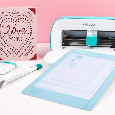 Cricut Joy machine is pictured with a ''Love You" greeting card and Cricut mat and tools