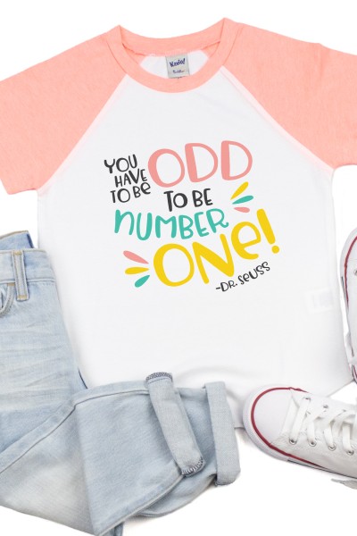 Pair of blue jeans, sneakers and a baseball style shirt that is pink and white.  The shirt has a quote that says, "You have to be odd to be number one! - Dr. Seuss