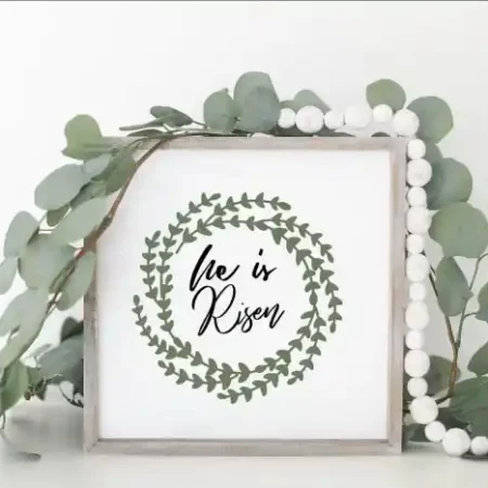 Framed white sign with image of a laurel wreath the the words, He is Risen