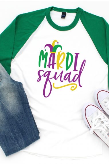 Pair of blue jean shorts and tennis shoes along with a baseball style shirt that is white with green sleeves. The white section of the shirt has a design for Mardi Gras that says, "Mardi Squad".