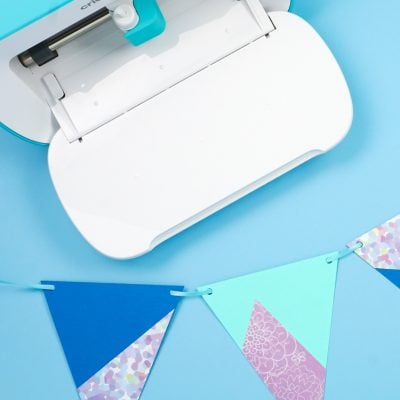 Cricut Joy machine with a banner of pennants lying next to it.  The pennants are cut out of regular cardstock and adhesive backed paper.