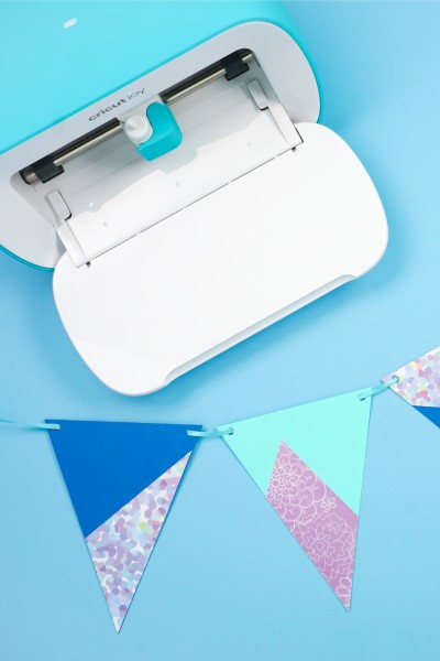 Cricut Joy machine with a banner of pennants lying next to it.  The pennants are cut out of regular cardstock and adhesive backed paper.