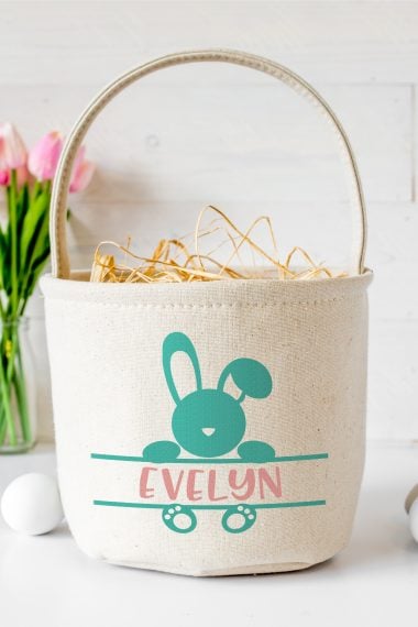 Easter Bunny Monogram on a canvas style basket, personalized with child's name.  Picture background includes a vase of pink tulips and a white egg next to the basket.