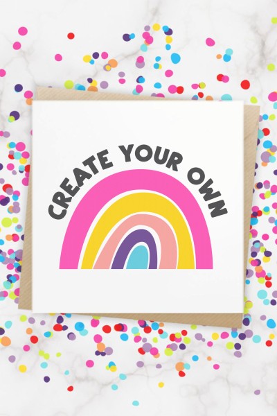 Close up of a rainbow with the words "Create Your Own" over the curve of the rainbow.  This design is on a white sheet of paper and the paper is surrounded by colorful confetti
