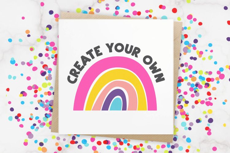 Close up of a rainbow with the words \"Create Your Own\" over the curve of the rainbow.  This design is on a white sheet of paper and the paper is surrounded by colorful confetti