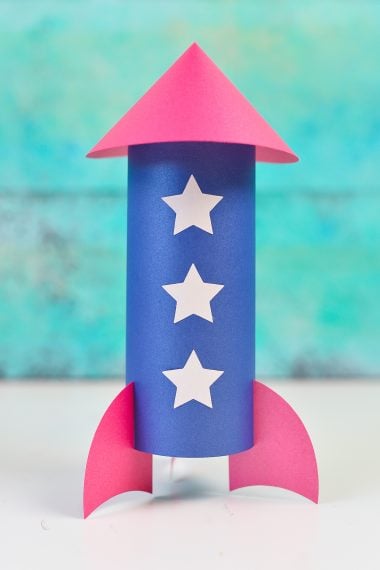 Picture of a paper rocket made out of red, white and blue paper that is sitting on a table