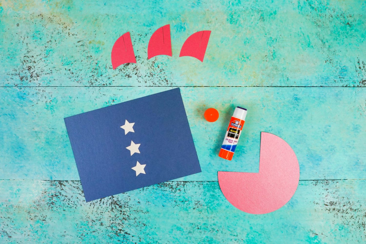 Image of the cutouts made from Cricut for the 4th of July Paper Rockets and a stick of Elmer\'s glue.  The star cutouts are glued to the body of the rocket.