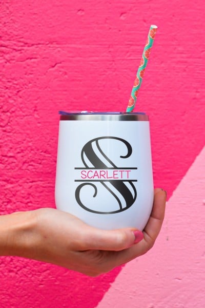 A person holding a tumbler with a straw.  Tumbler contains a design on it of a split monogram of the letter 'S' and the name Scarlett.