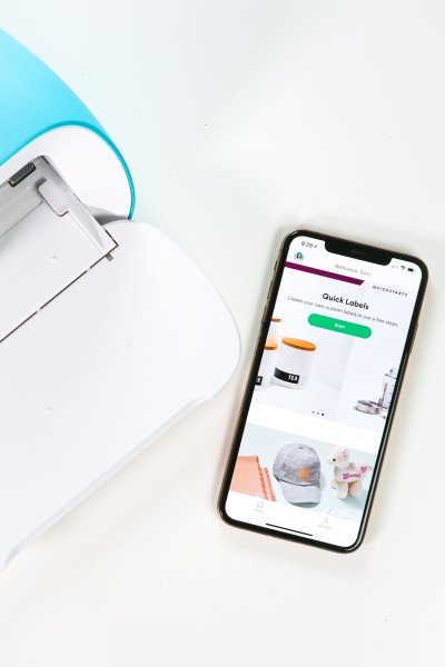 Image of the Cricut Joy machine and a cell phone sitting on table with the phone displaying the Cricut Joy App