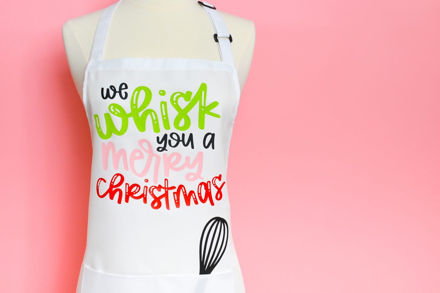 White apron with "We Whisk You a Merry Christmas" on pink background.