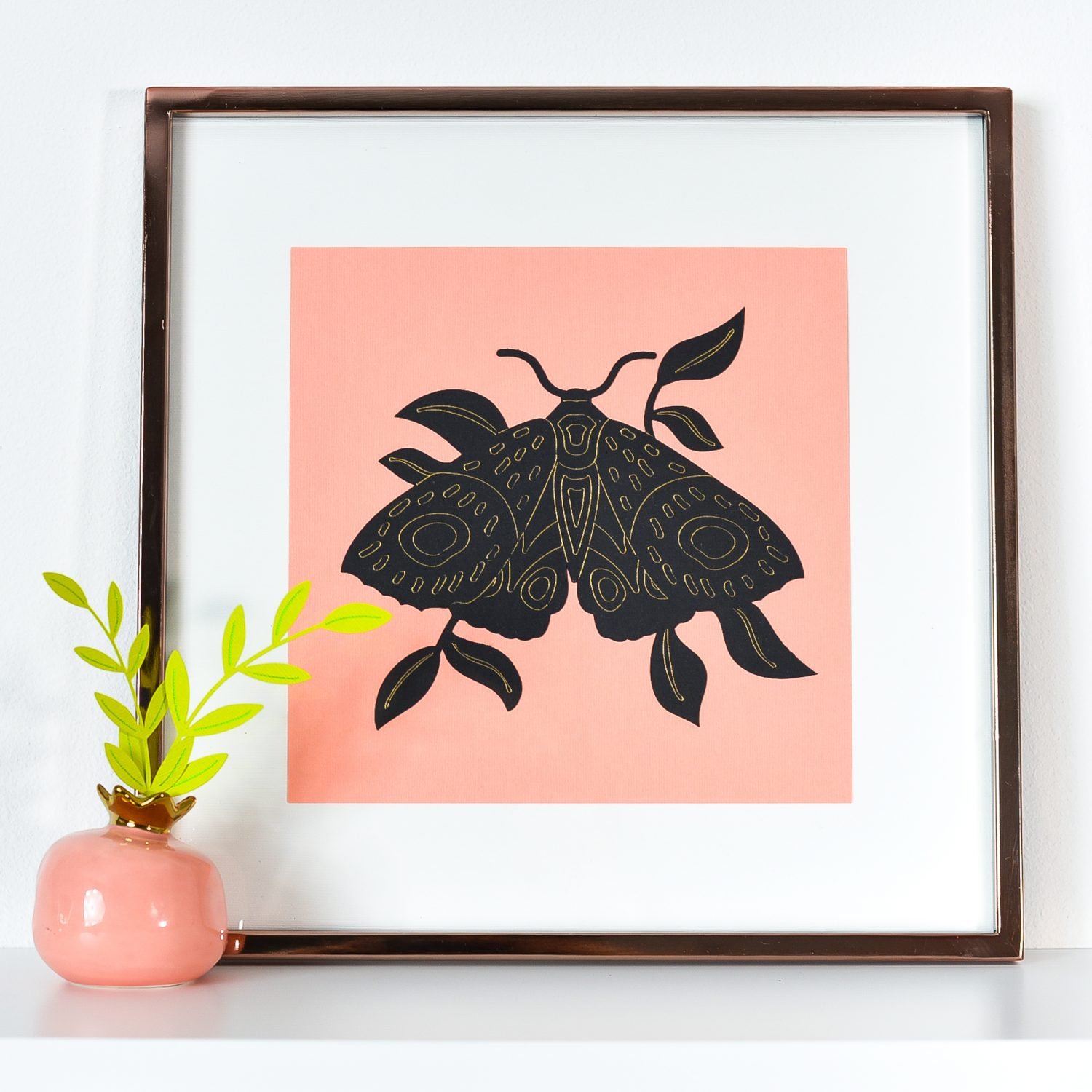 Image of a framed picture of a black butterfly against a pink background with a white mat.  Butterfly is enhanced with gold foil.