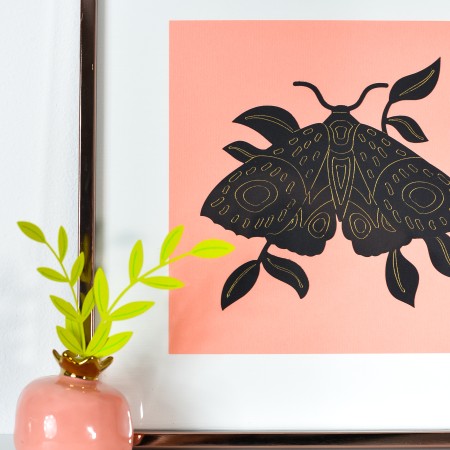 Moth artwork on shelf with small paper plant