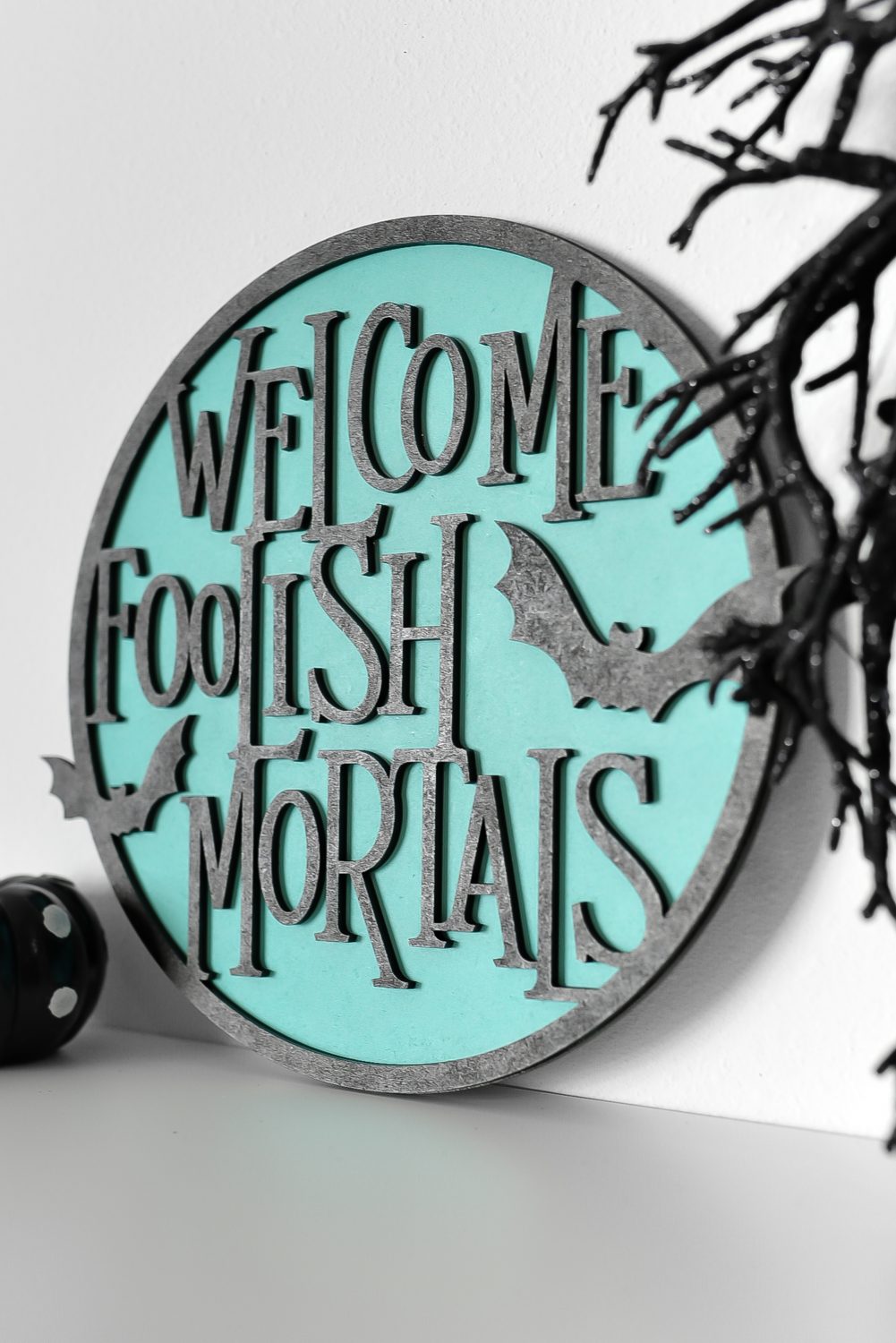 Angled shot of Welcome Foolish Mortals sign on a shelf with Halloween decor