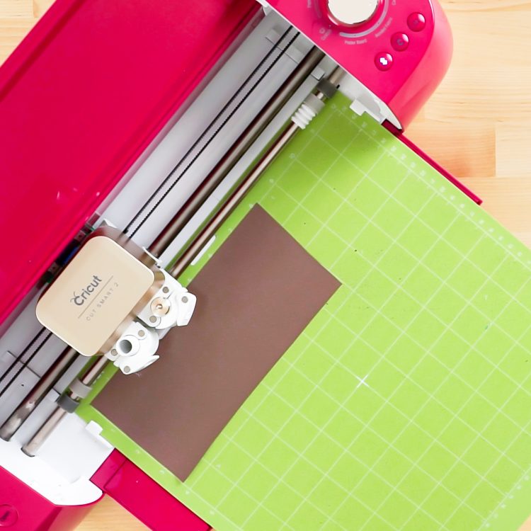 Image of Cricut machine cutting out a design on brown vinyl that is pressed onto the green Cricut mat.