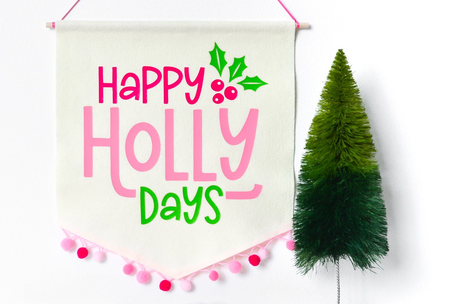 Image of the completed Happy Holly Days Christmas Banner hanging on the wall and near a small fake green tree