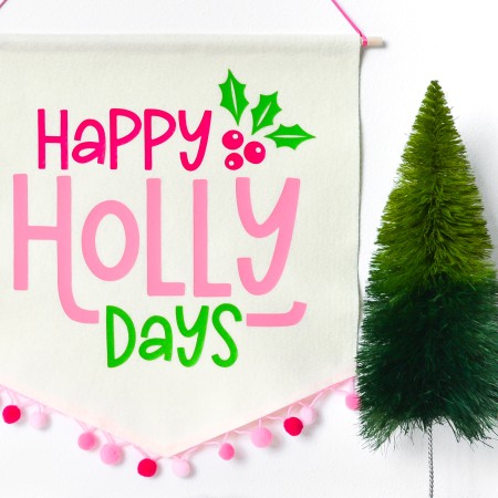 Image of the completed Happy Holly Days Christmas Banner hanging on the wall and near a small fake green tree