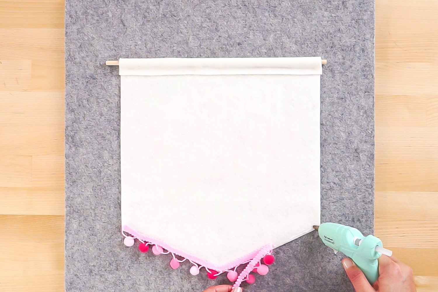 Gluing the pom pom trim onto the felt Christmas banner.