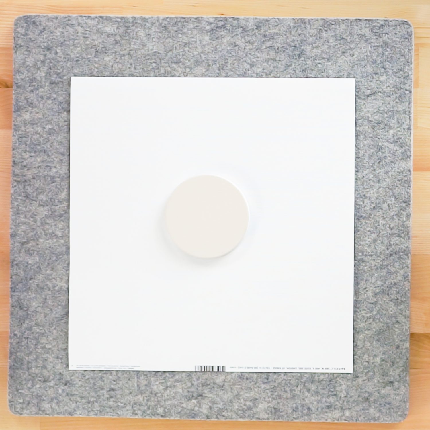 Image of a Cricut Mat with a piece of white cardstock on top of the mat and a snowflake design on top of the cardstock and an off-white coaster on top of the design