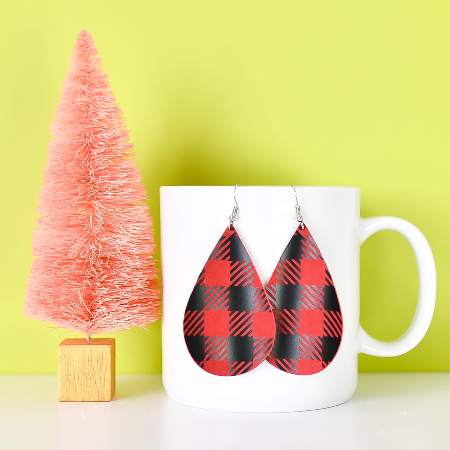 Finished buffalo plaid earrings hanging from a mug.