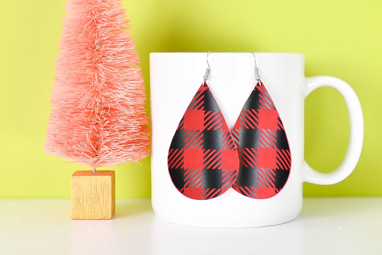 Finished red buffalo plaid earrings hanging from a coffee cup