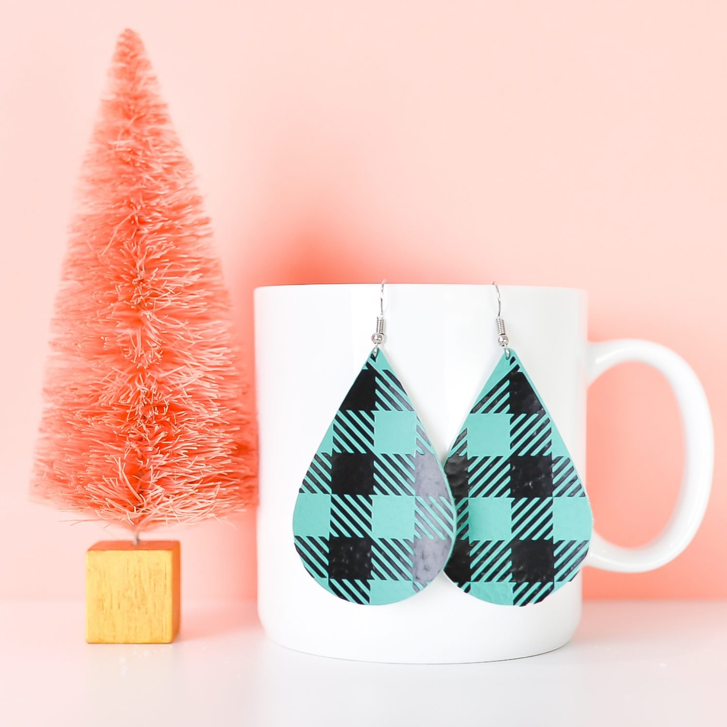 Finished teal buffalo plaid earrings hanging from a coffee cup