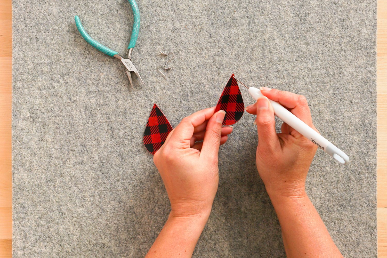 Hands using the piercing tool to create a hole at the top of the earring.