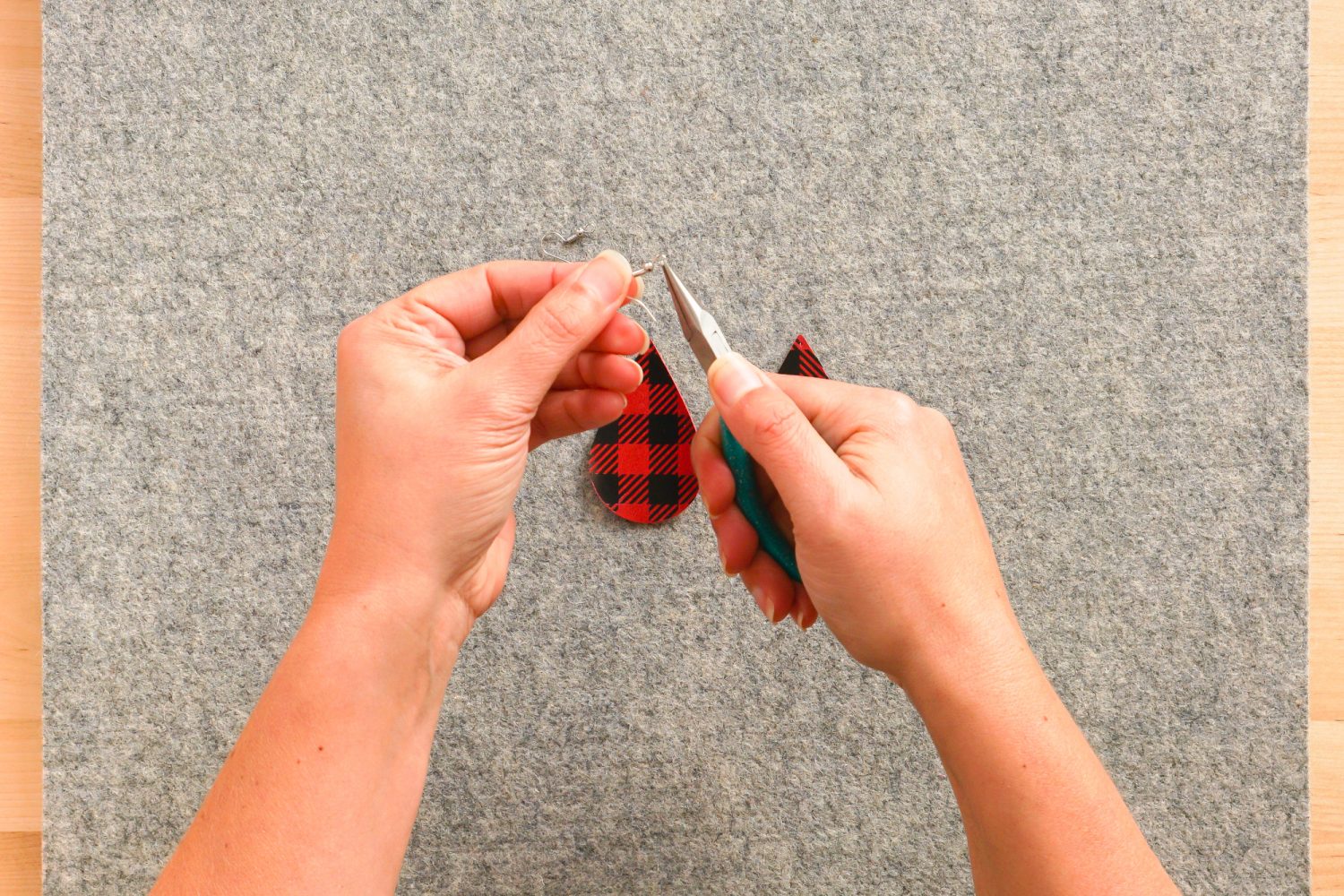 Hands using the pliers to open the ring on the earring finding.