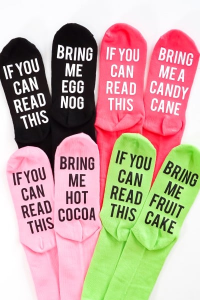 Image of Christmas socks in black, red, pink and neon green colors with the following sayings:  One sock of each pair says, "If you can read this" and the partner of each one says either, "Bring Me Egg Nog", or "Bring Me Candy", or Bring Me Hot Cocoa", or "Bring me Fruit Cake"