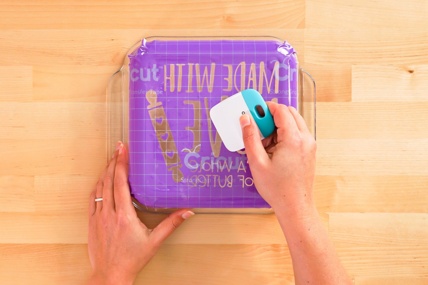 Hands using the scraper to burnish the stencil to the dish.