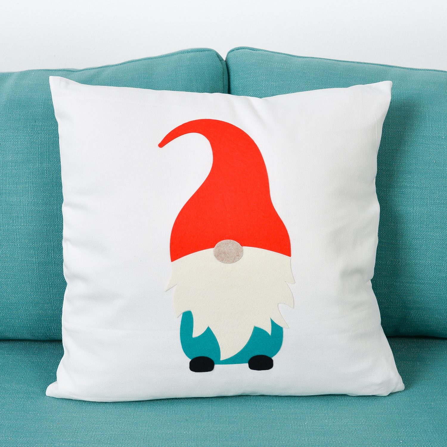 Felt gnome pillow sitting on a blue couch.