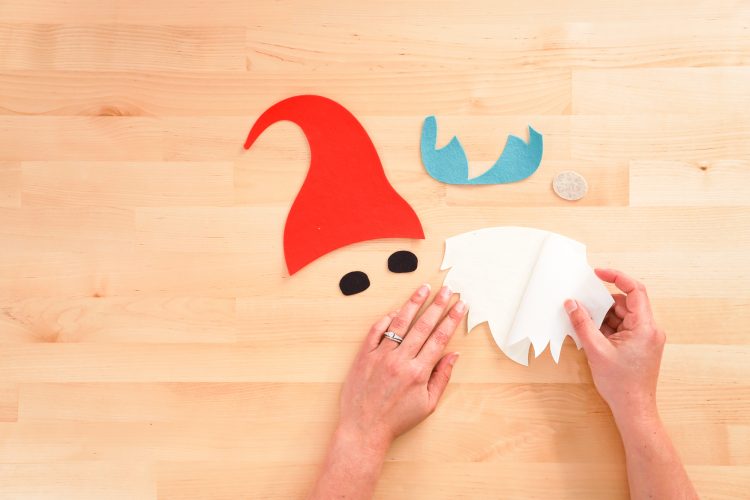 Displaying the cut out felt pieces used for the Gnome pillow with woman peeling peel back the backing sheet on the HeatnBond to reveal the shiny, heat-reactive adhesive