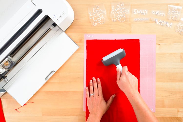 Hands using a brayer to put red flannel on Cricut mat