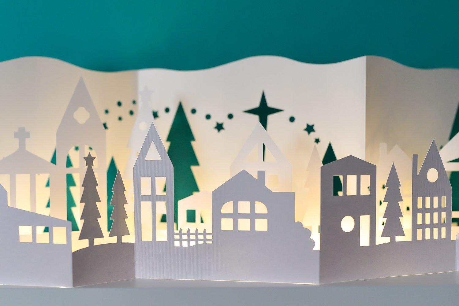 Close up image of Papercut Christmas Village on a shelf illuminated with fairy lights