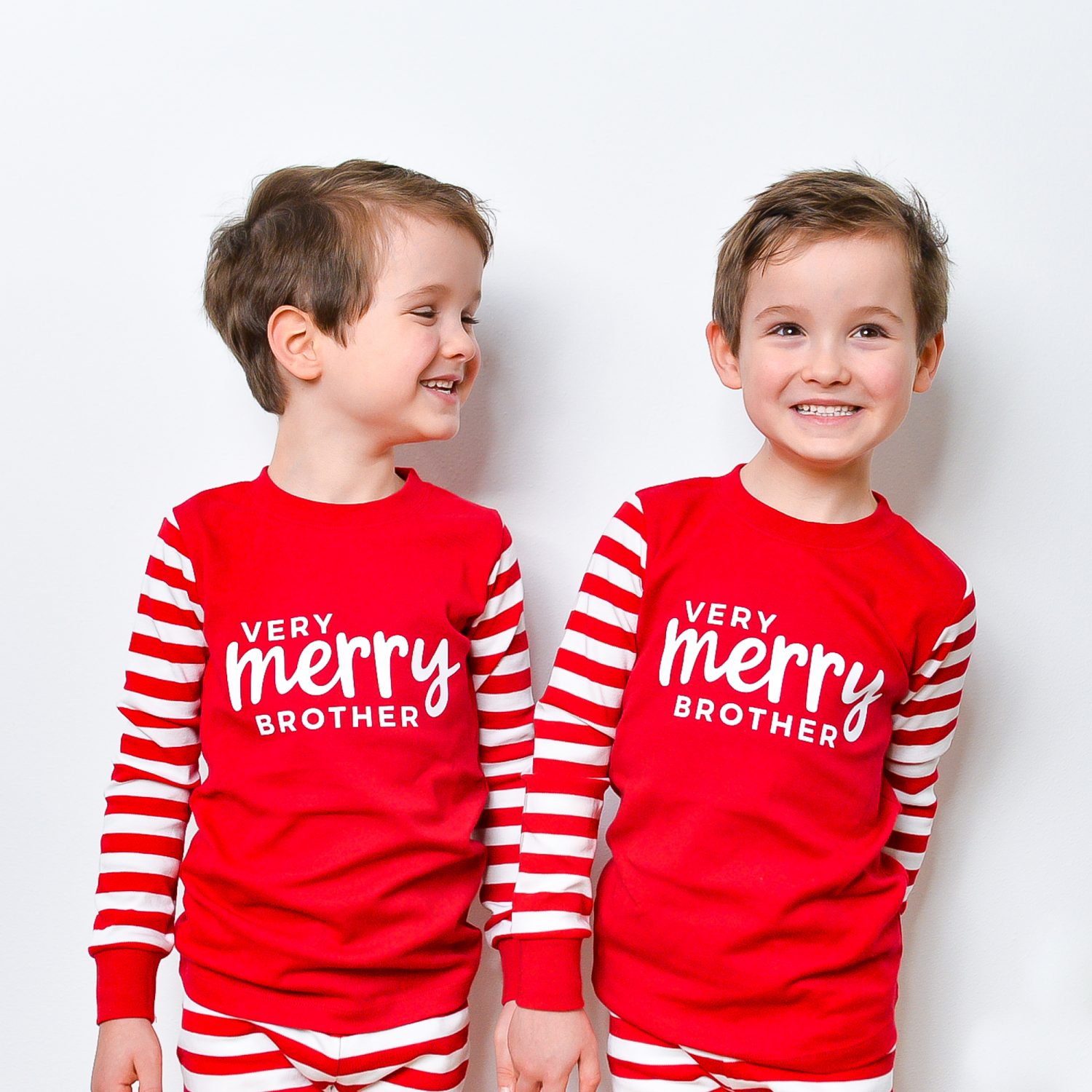 Two young boys in red and white striped pajamas with \"Very Merry Brother\" displayed on the pajama tops