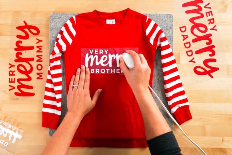 Hands ironing Very Merry Brother decal to shirt