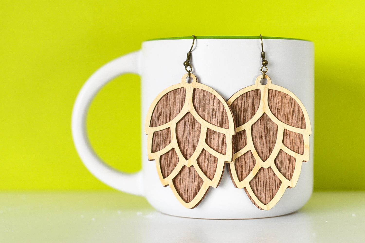 Finished pinecone earrings hanging from a mug with a green background.