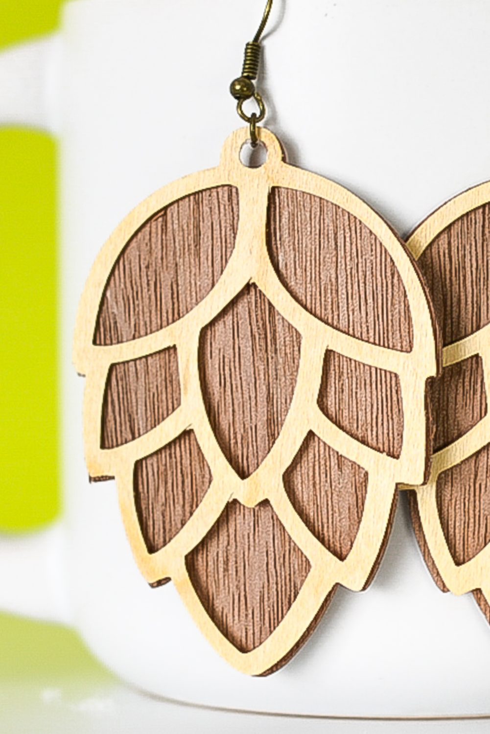 Close up of finished pinecone earrings hanging from a mug with a green background.