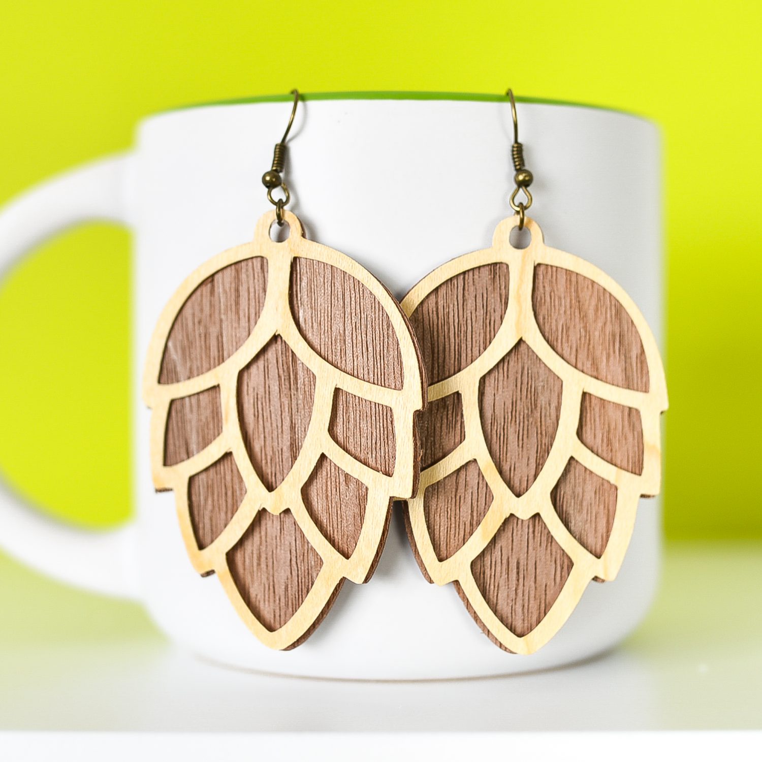 Close up of finished pinecone earrings hanging from a mug with a green background.