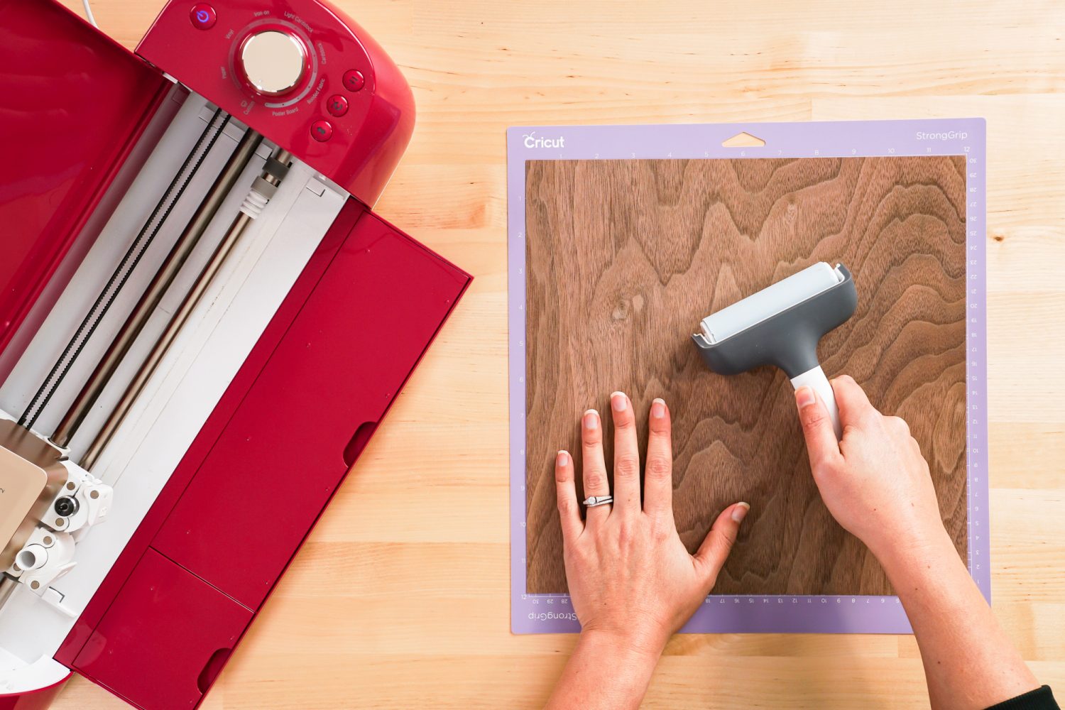 Hands using a brayer to place the veneer on a Cricut mat.