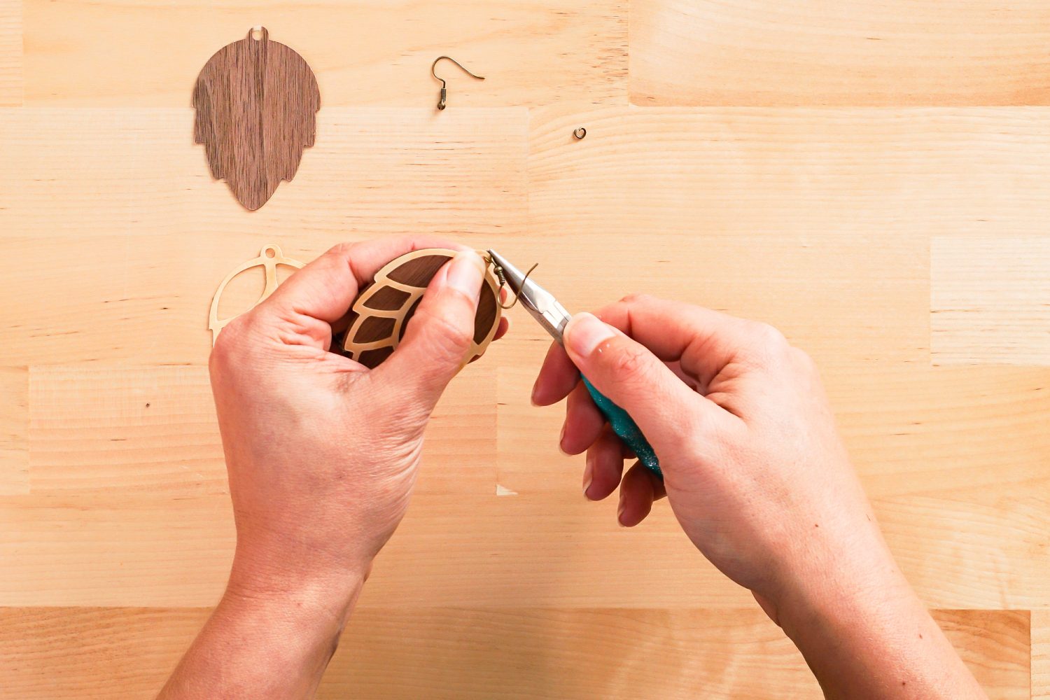 Hands clamping the jump ring closed with the pliers.