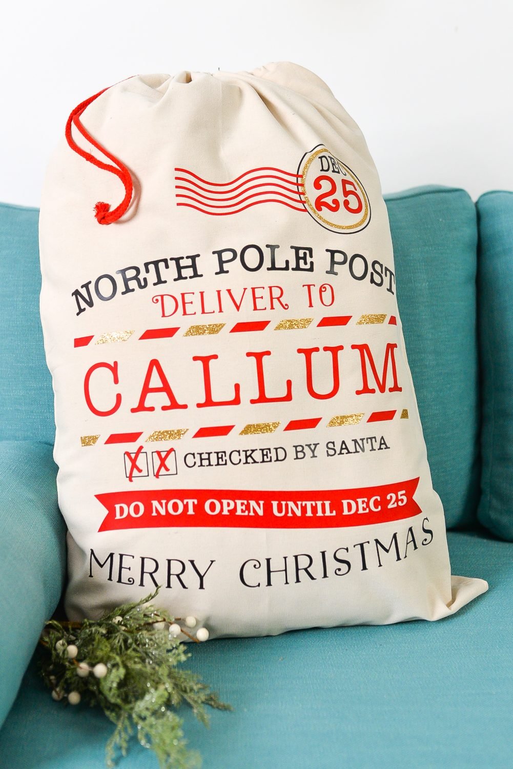 Picture of a personalized gift filled Santa Sack sitting on an aqua colored sofa.