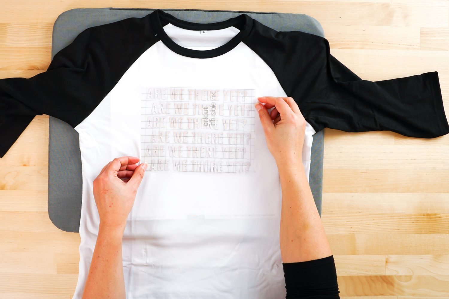 Hands placing the Infusible Ink decal on the raglan.